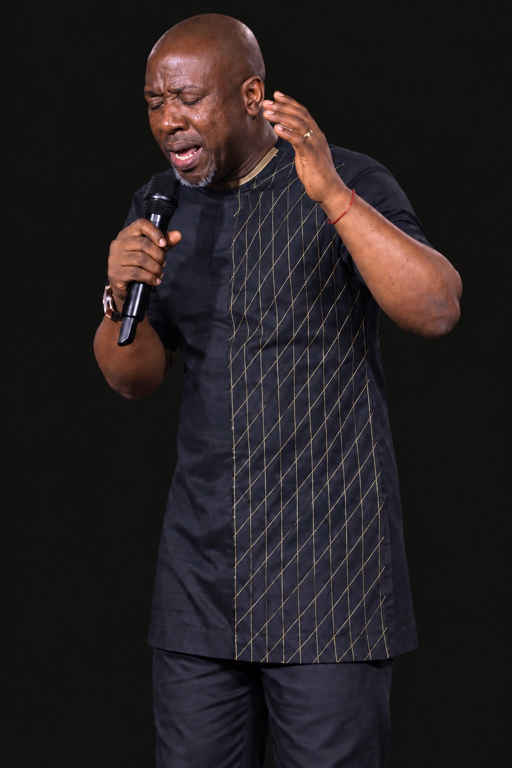 A man holding a microphone with his eyes closed and one hand raised.